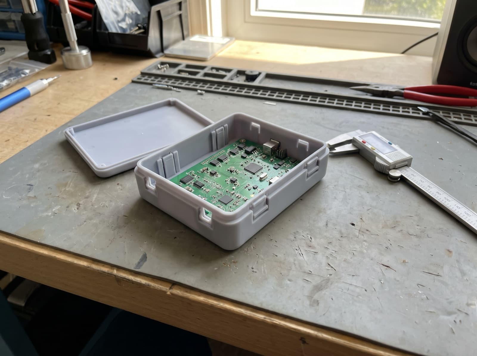 Gri reçineden basılmış, içinde elektronik kart bulunan geçme kapaklı muhafaza prototipi ve kumpas